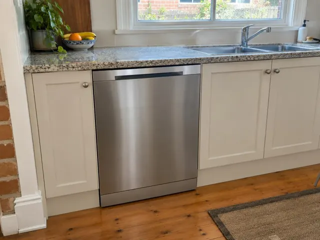Stainless dishwasher installed under a stone benchtop in a cream kitchen with window and sink in Carrington