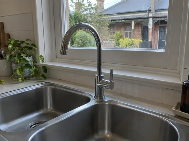 Kitchen sink with chrome mixer tap beneath a window in a tiled home kitchen in Maryville