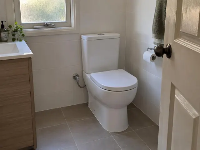 White toilet in a tiled bathroom beside a vanity and window in Newcastle West